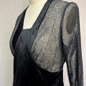 以下が含まれることがあります： 黒いベルベットのドレスと、透け感のあるレースのオーバーレイ。 ドレスはスクエアネックと長袖が特徴です。 レースのオーバーレイには繊細な花柄があります。 ドレスはマネキンに展示されています。
