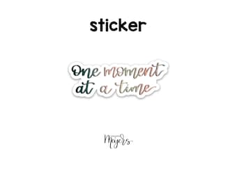 May include: A sticker with the text "One moment at a time" in a gradient of pink and green. The sticker is from the company "moments mayers".