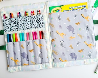 May include: An open activity book with a gray and white animal print cover. The book has two pockets on the left side, one with a leopard print and the other with a gray and white animal print. The pockets hold colored pencils and markers. The book also has a pocket on the right side for a coloring book. The book is labeled "3-in-1 Activity Puzzle Book".