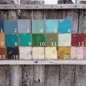 May include: A collection of twenty-two small, square wooden blocks, each painted a different color. The colors range from dark blue to light pink, with numbers 1 through 22 printed on each block. The blocks are arranged on a weathered wooden surface.
