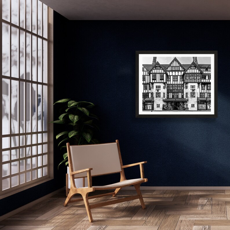 May include: A black and white photograph of a building with a large storefront. The building has a traditional design with multiple windows and a flat roof. The photograph is framed in a black frame and is hanging on a dark blue wall.