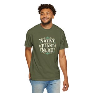Könnte beinhalten: Ein grünes T-Shirt mit einer weißen Grafik, auf der "Native Plant Nerd" in einer Vintage-Schriftart mit grünen floralen Akzenten steht.