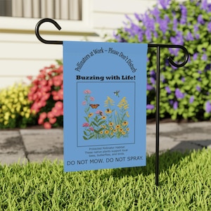 Op de afbeelding: Blauwe tuin vlag met een kolibrie en een vlinder die over een bloemenveld vliegen. De tekst op de vlag luidt "Pollinators at Work - Please Don't Disturb Buzzing with Life! Protected Pollinator Habitat These native plants support local bees, butterflies, and birds. DO NOT MOW. DO NOT SPRAY."