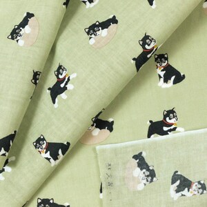 May include: Green fabric with a repeating pattern of black and white Shiba Inu dogs. Some dogs are lying down, while others are standing and looking to the right. The fabric is folded in half, showing the pattern on both sides.