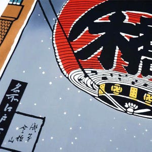 May include: Close-up of a Japanese-style illustration featuring a large red and black lantern with Japanese characters. The background is a light blue with white dots, and there is a small section of a building in the upper left corner.