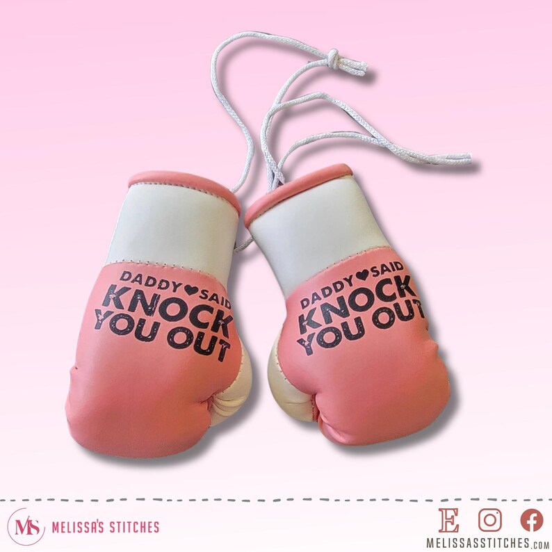 Pu&ograve; includere: Due guantoni da boxe rosa e bianchi con la scritta "DADDY SAID KNOCK YOU OUT" in nero. I guantoni sono collegati da uno spago bianco. I guantoni hanno una combinazione di colori rosa e bianco.