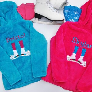 Könnte beinhalten: Zwei Fleecejacken mit einem personalisierten Design von Schlittschuhen und den Namen "Bristol" und "Skylar", die darauf gestickt sind. Die Jacken sind türkis und pink.