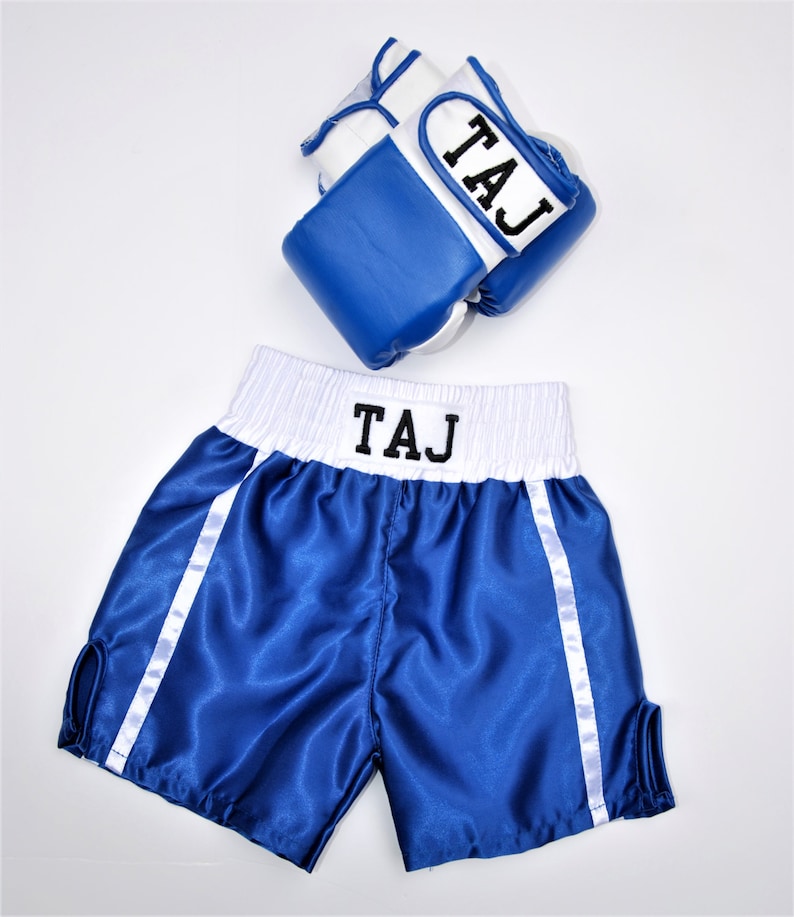 May include: Blue and white boxing shorts with white piping and the name "TAJ" embroidered on the waistband. A pair of blue and white boxing gloves with the name "TAJ" embroidered on the wrist strap.