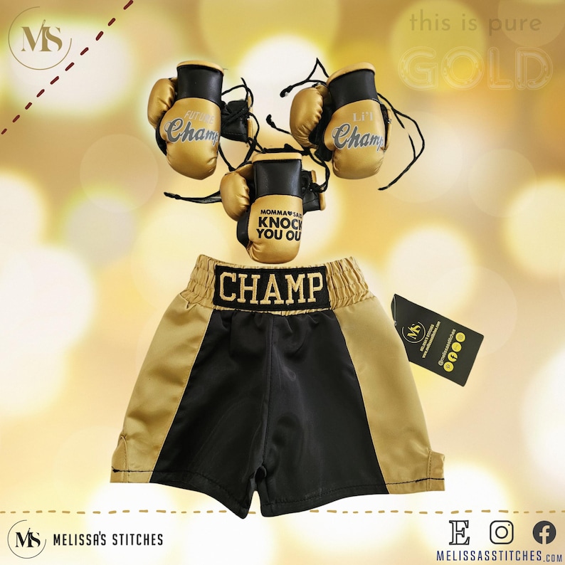K&ouml;nnte beinhalten: Goldene Boxershorts mit schwarzem Besatz und dem gestickten Wort "CHAMP" am Bund. Drei goldene Mini-Boxhandschuhe mit den gestickten Worten "Lil Champ" und "Momma's gonna knock you out".