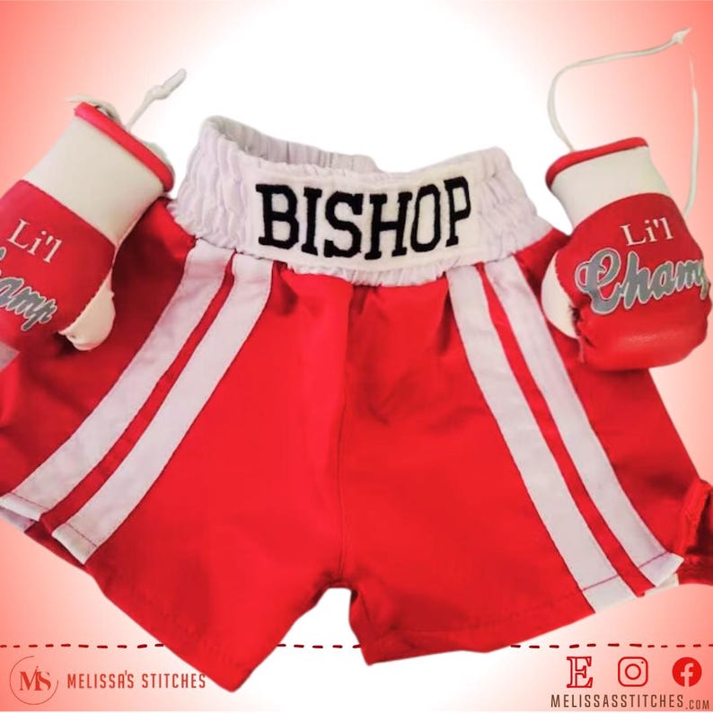 K&ouml;nnte beinhalten: Rote und wei&szlig;e Boxershorts mit dem Namen "BISHOP" auf dem Bund gestickt. Die Shorts werden mit einem Paar wei&szlig;en Boxhandschuhen geliefert, auf denen der Text "Lil Champ" gestickt ist.