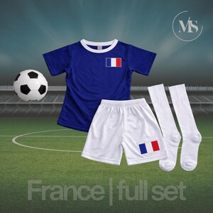 May include: A blue soccer uniform set with the French flag emblem, including a jersey, shorts, and socks. A soccer ball is on the left. The words "France | full set" are at the bottom.