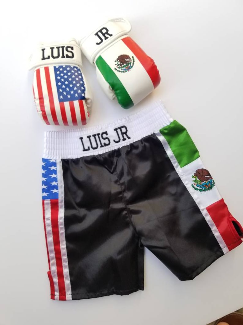 May include: Black satin boxing shorts with American and Mexican flag accents. The shorts have the name "LUIS JR" embroidered on the waistband. Two white boxing gloves with the names "LUIS" and "JR" and the American and Mexican flags are also pictured.