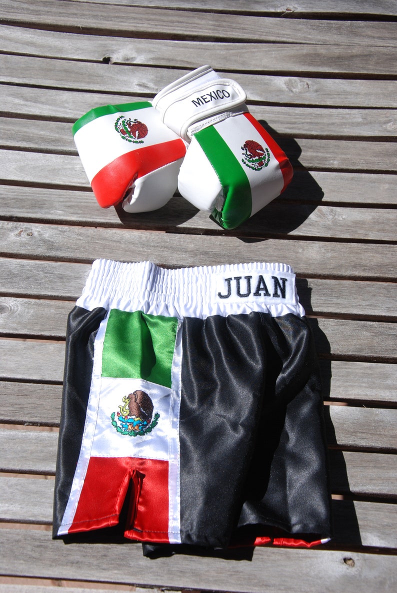 May include: Black and green boxing shorts with a white waistband and the word "JUAN" embroidered on the waistband. The shorts have a Mexican flag design with a green, white, and red color scheme.