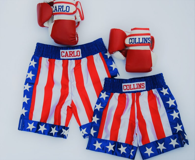 May include: Two pairs of red and white boxing gloves with blue trim and the names "CARLO" and "COLLINS" on them. Two pairs of red, white, and blue boxing shorts with stars and stripes.
