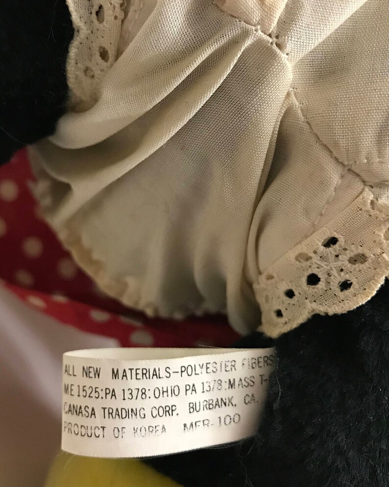 K&ouml;nnte beinhalten: Ein wei&szlig;es Etikett mit schwarzem Text, der "ALL NEW MATERIALS-POLYESTER FIBERS ME 1525:PA 1378: OHIO PA 1378:MASS T- CANASA TRADING CORP. BURBANK, CA. PRODUCT OF KOREA MER. 100" lautet.