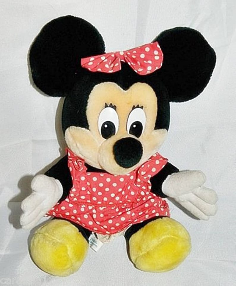 K&ouml;nnte beinhalten: Ein Pl&uuml;schtier von Minnie Mouse, die ein rot-wei&szlig; gepunktetes Kleid mit einer roten Schleife tr&auml;gt. Sie hat gro&szlig;e schwarze Ohren und gelbe Schuhe.