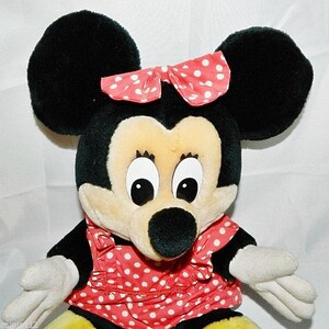 K&ouml;nnte beinhalten: Ein Pl&uuml;schtier von Minnie Mouse mit schwarzen Ohren, einer roten Schleife mit wei&szlig;en Punkten und einem roten Kleid mit wei&szlig;en Punkten.