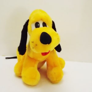 Peut inclure: Un chien en peluche jaune avec des oreilles noires et un nez noir. Le chien est assis les pattes repliées sous son corps.