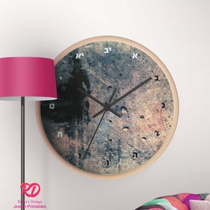 Puede incluir: Un reloj de pared redondo con un fondo texturizado y desgastado. La esfera del reloj presenta números hebreos y manecillas negras. El reloj tiene un marco de madera.