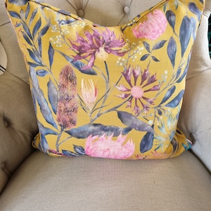 May include: A yellow throw pillow with a floral pattern featuring pink, purple, and blue flowers. The pillow has a subtle linen texture.