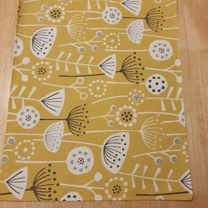 Könnte beinhalten: Ein gelber Platzdeckchen mit einem weißen und grauen Blumenmuster. Das Platzdeckchen hat ein schlichtes, modernes Design mit stilisierten Blumen und Stielen.