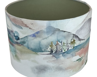 May include: A watercolor-style lampshade featuring a landscape scene with mountains, trees, and a lake. The shade has a light green interior and a white fabric exterior.