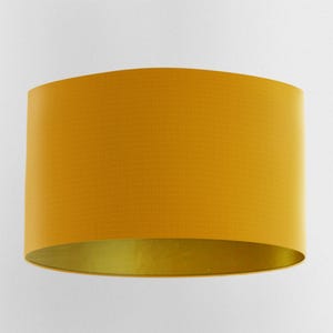 Könnte beinhalten: Ein gelber Trompetenschirm mit goldener Innenverkleidung. Der Lampenschirm ist aus Stoff und hat eine glatte, gleichmäßige Textur.