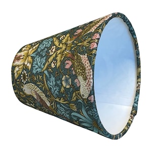 May include: A lampshade with a botanical design featuring birds, flowers, and foliage in teal, gold, and pink. The lampshade has a tapered shape and a white interior.