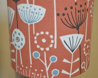 May include: A lampshade with a floral pattern in shades of orange, blue, and white. The lampshade is made of fabric and has a cylindrical shape.