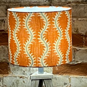 May include: Orange lampshade with a white and gray geometric pattern. The lampshade is on a wooden tripod stand.