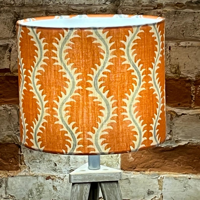 May include: Orange lampshade with a white and gray geometric pattern. The lampshade is on a wooden tripod stand.