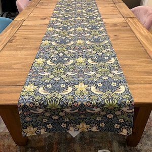 Könnte beinhalten: Ein blauer Tischläufer mit einem sich wiederholenden Muster aus stilisierten Vögeln, Blumen und Blättern. Das Muster ist in den Farben Gelb, Grün, Rosa und Weiß gehalten.