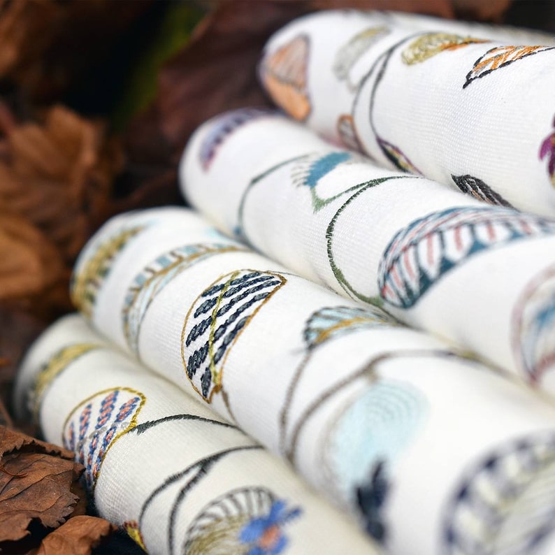 May include: A stack of white fabric tea towels with a colourful floral pattern. The towels are folded and stacked on top of each other. The pattern features leaves and flowers in shades of blue, green, yellow, and orange.