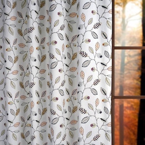 May include: White fabric with a repeating pattern of brown, black, and green leaves on branches. The fabric is shown hanging in front of a window with a blurry background of autumn foliage.