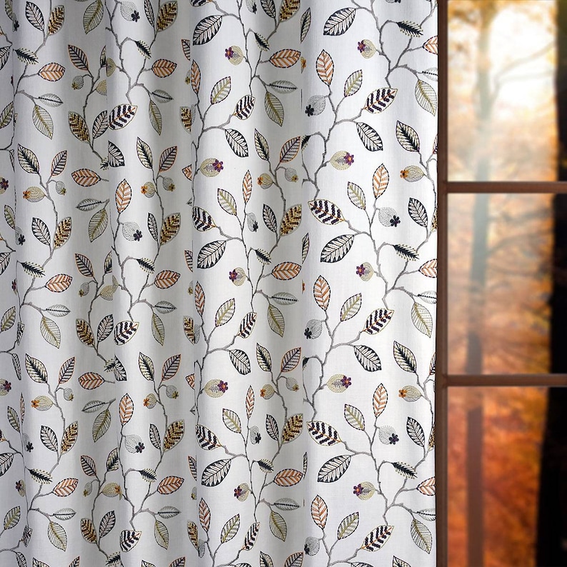 May include: White fabric with a repeating pattern of brown, black, and green leaves on branches. The fabric is shown hanging in front of a window with a blurry background of autumn foliage.