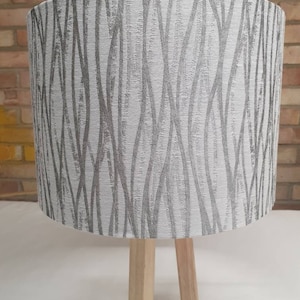 May include: A white lampshade with a gray abstract pattern, on a wooden tripod base.