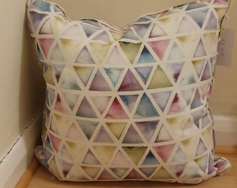 May include: A white pillow with a geometric pattern of colorful triangles. The triangles are in shades of pink, blue, green, and purple. The pillow has a white background and a subtle watercolor effect.