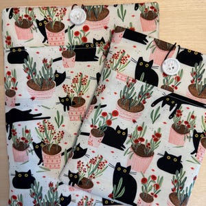 May include: Two fabric pouches with black cats and red flowers on a white background. The pouches have a button closure and are made of a soft, durable fabric.