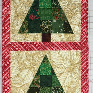 May include: A rectangular quilted table runner featuring four square panels, each displaying a patchwork Christmas tree in shades of green with a brown trunk, set against a cream-colored background with gold leaf patterns and red borders.