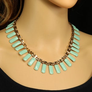 May include: A mint green and gold-tone necklace. The necklace features rectangular mint green enamel pendants connected by a gold-tone chain. The necklace is displayed on a mannequin.