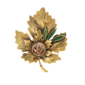 May include: A vintage-style leaf brooch with a gold-tone finish. The brooch features a detailed leaf design with a central, clear, round stone. Green enamel accents the leaves, adding a pop of color to the piece. A classic accessory.