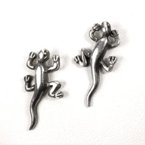 May include: Two silver-toned lizard-shaped pins or ornaments with smooth, reflective surfaces. Each lizard is depicted in a climbing position with four legs extended and a long, curved tail. The metallic figures have simple, rounded features.
