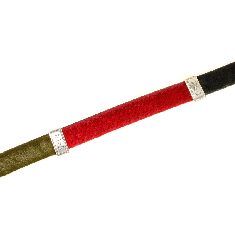 Puede incluir: Un collar gargantilla colorido con una secci&oacute;n central roja, flanqueada por segmentos verde oliva y negros. El collar presenta cierres rectangulares plateados con detalles decorativos. El collar probablemente est&aacute; hecho de un material suave y texturizado.