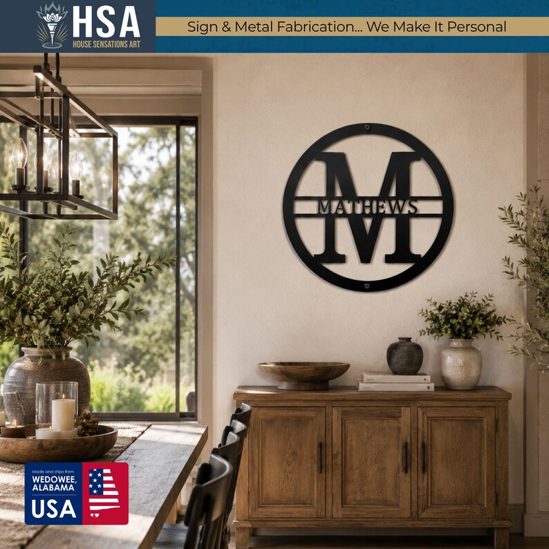 Personalized round black metal monogram sign with family name, mounted on wall above a wooden console in a bright entryway.