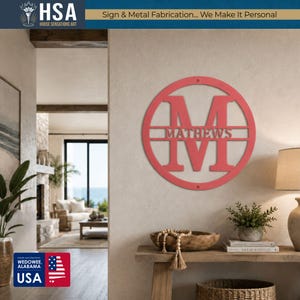 Personalized circular pink metal monogram door sign with a large M and family name, wall-mounted entrance decor.