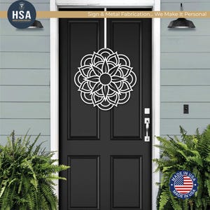 White metal mandala door wreath on a black front door; geometric floral wall art for outdoor front door decor.