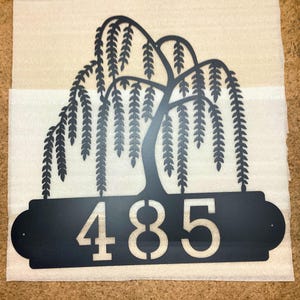 Weeping Willow House Numbers Plaque shown in Black with Example Street Numbers. Item is laying on packing materials prior to shipment