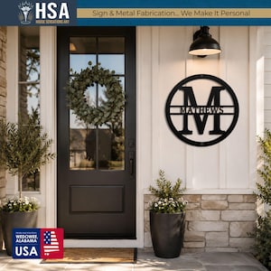 Personalized round black monogram family name sign on front entrance wall; MATTHEWS with wreath and potted plants nearby.