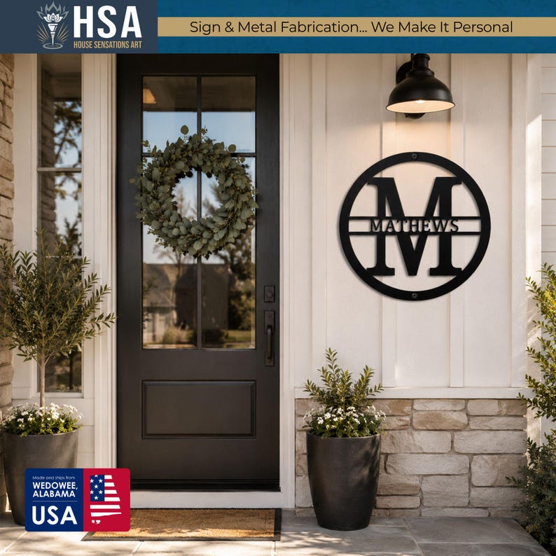 Personalized round black monogram family name sign on front entrance wall; MATTHEWS with wreath and potted plants nearby.