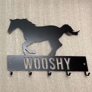 May include: Black metal horse silhouette wall mounted key holder with the name "WOOSHY" cut out below the horse. The key holder has five hooks.